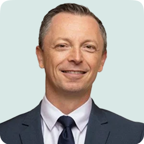 Professional headshot of a middle-aged man in a navy-blue suit and tie, smiling confidently.
